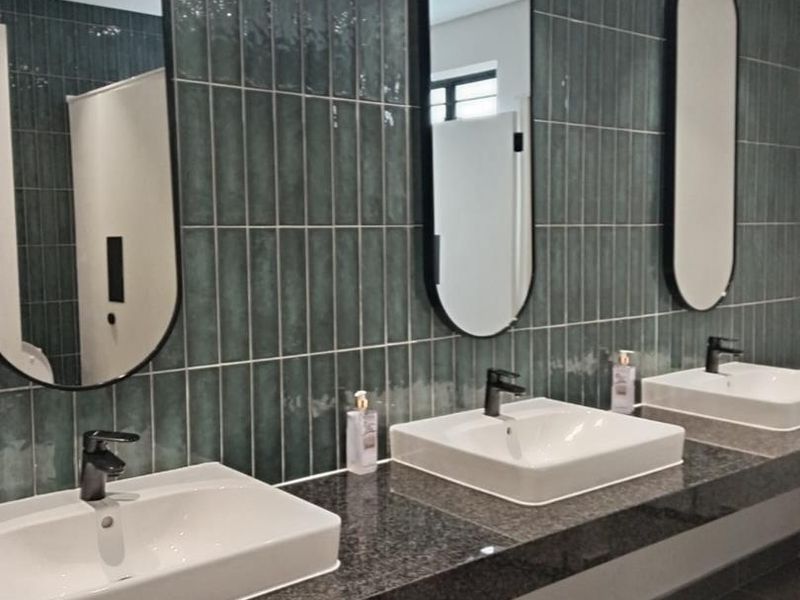 Modern industrial-style bathroom featuring a triple vanity with granite countertop, ceramic vessel sinks, black matte fixtures, and stylish vertical teal subway tiling.