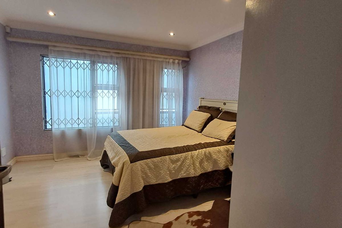 A bedroom featuring light-toned laminate flooring, recessed ceiling lighting, and window security bars.