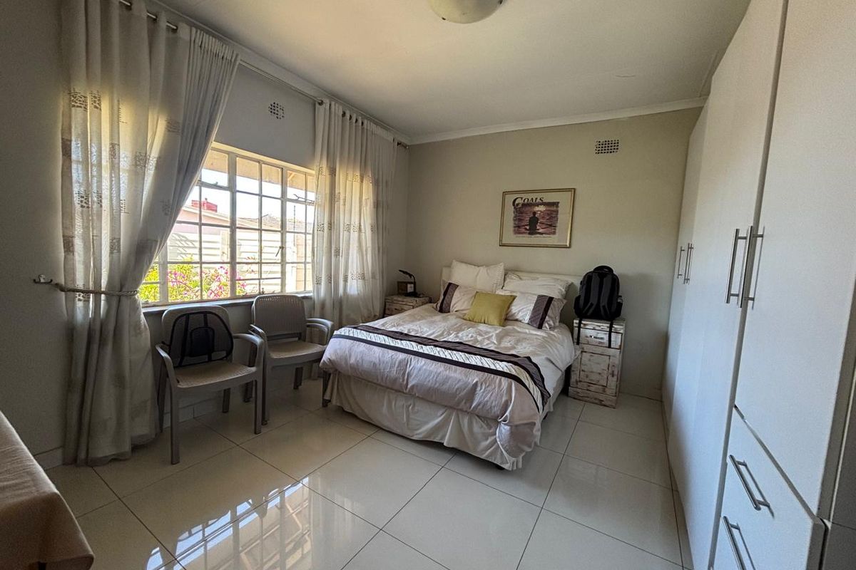 A well-lit bedroom featuring large format floor tiles, built-in wardrobes, and a window with natural light.