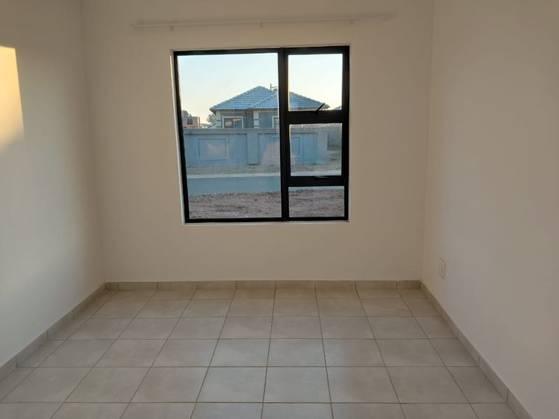 A clean, empty bedroom featuring neutral tiled flooring and a modern black aluminium window frame, providing a blank canvas for personalization.