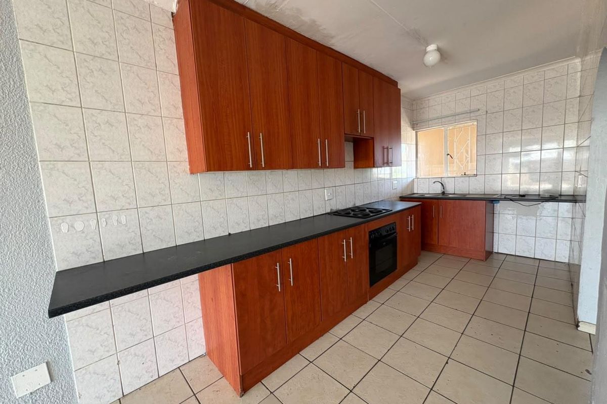 A functional kitchen featuring wood-look cabinetry, dark countertops, built-in oven and hob, and tiled finishes, currently vacant and ready for updates.
