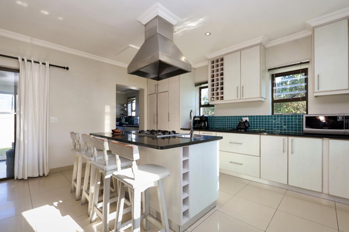 Modern kitchen featuring a central island with a built-in gas hob, stainless steel extractor fan, granite countertops, and tiled backsplash.