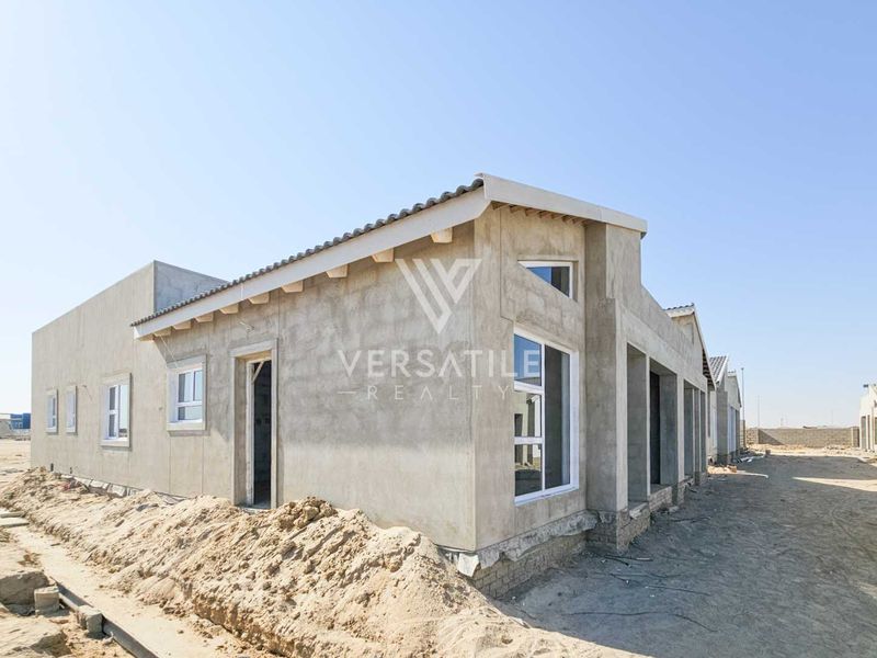 Exterior view of a townhouse under construction, featuring raw concrete walls, tiled roofing, and installed aluminium window frames on an unlandscaped plot.