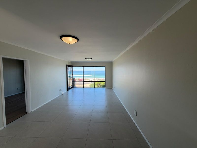 Spacious, empty living area featuring neutral tiled flooring, coved ceilings, and a large glass sliding door offering direct ocean views.