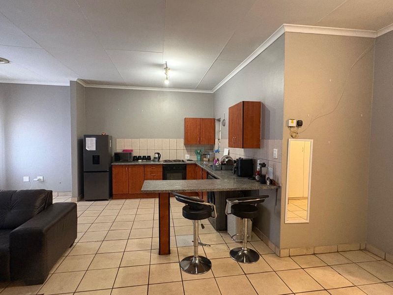 Open-plan kitchen and living area featuring tiled flooring, wooden cabinetry, a breakfast bar, and built-in cooking appliances.