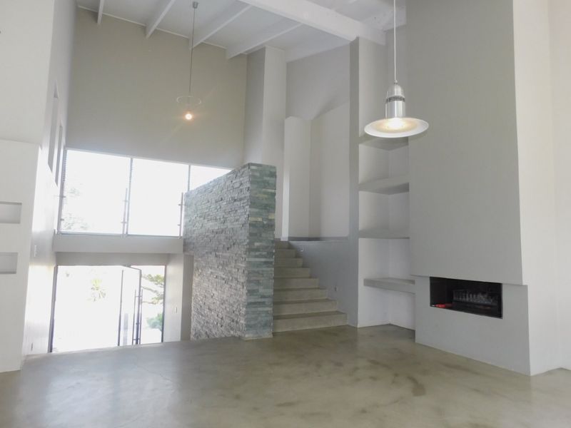 Spacious living area featuring high ceilings, exposed beams, a striking stone feature wall, built-in fireplace, and polished concrete flooring.