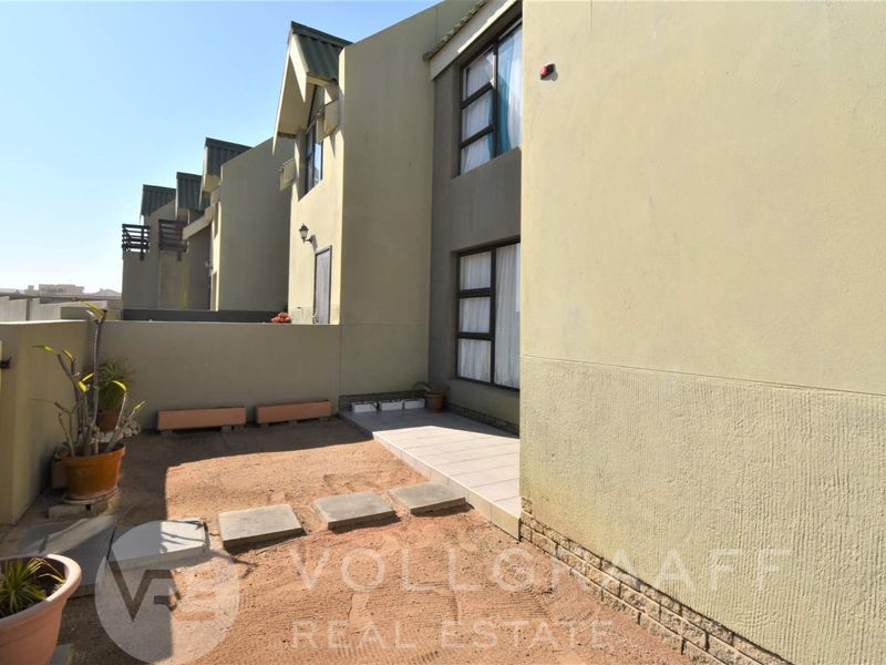 Rear exterior view of the townhouse featuring a small tiled patio area and a private garden space with boundary walling.