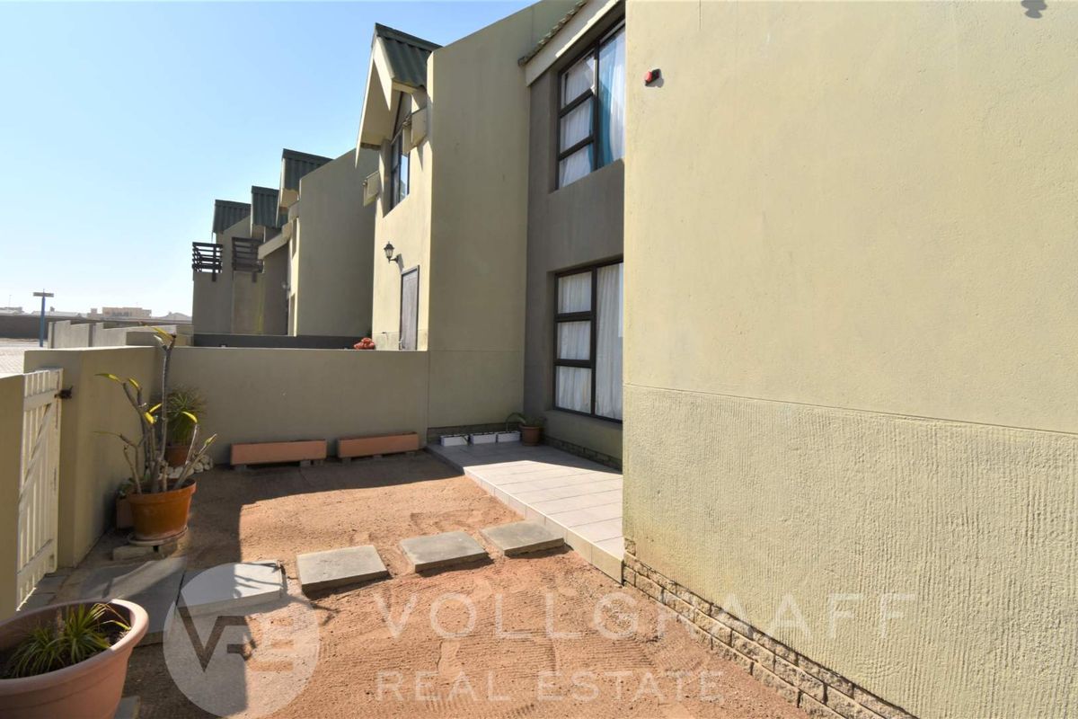 Rear exterior view of the townhouse featuring a small tiled patio area and a private garden space with boundary walling.