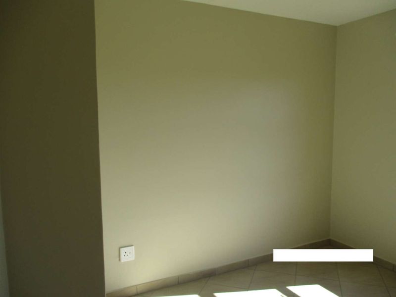 An empty bedroom featuring neutral painted walls, tiled flooring, and a standard electrical outlet.