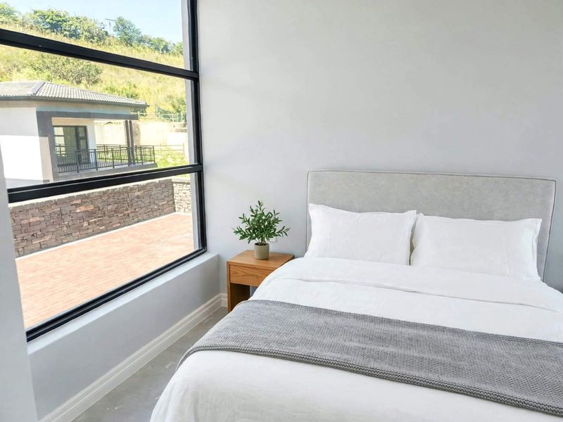 A bright, modern bedroom featuring a large floor-to-ceiling window that provides ample natural light and views of the exterior surroundings.