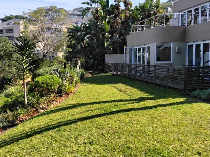 A well-maintained rear garden featuring a timber deck, stainless steel balustrade, and sliding glass doors leading into the apartment.