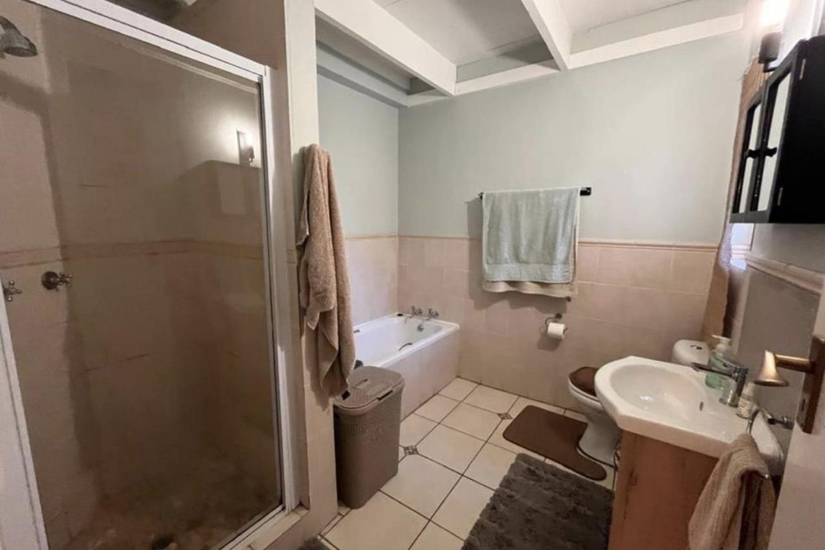 A functional bathroom featuring a separate shower enclosure, a built-in bathtub, a pedestal sink, and tiled flooring with neutral wall finishes.