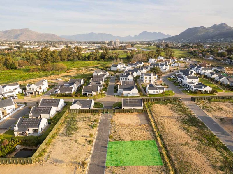 Aerial view of a vacant residential plot within a developed estate, featuring paved road access and surrounding established homes with mountain views.