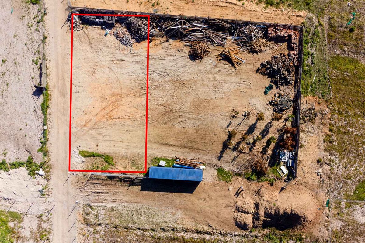 Aerial view of a vacant agricultural land plot featuring perimeter fencing and unpaved access, currently containing scattered debris and site materials.