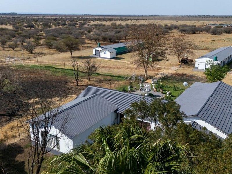 Aerial view of the farm property featuring multiple outbuildings, metal roof structures, and expansive surrounding landscape.