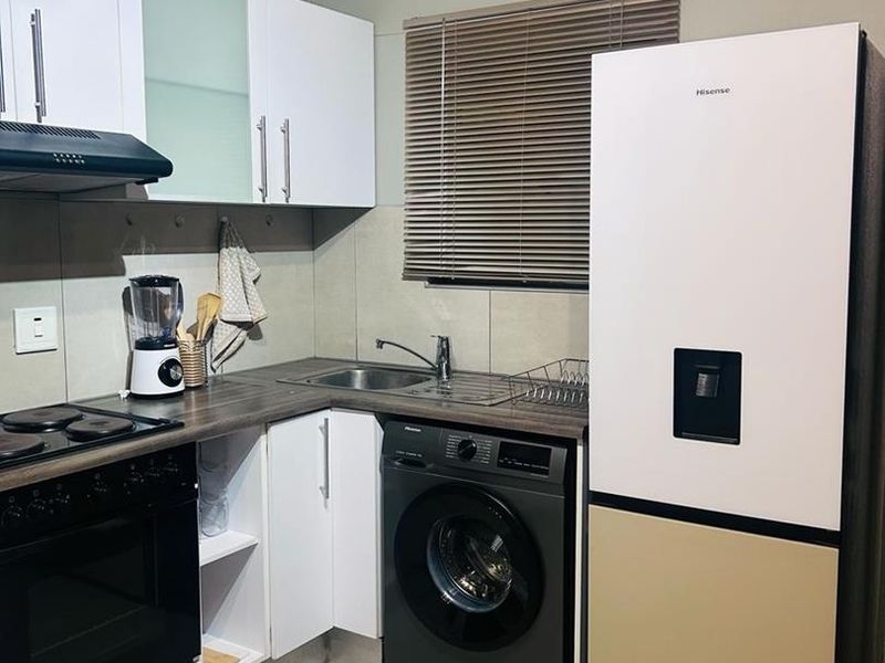 Compact modern kitchen featuring white cabinetry, dark laminate countertops, integrated oven and hob, and dedicated space for a washing machine.