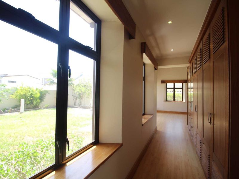 A bright, spacious hallway featuring extensive built-in wooden cabinetry, laminate flooring, and large windows overlooking the garden.