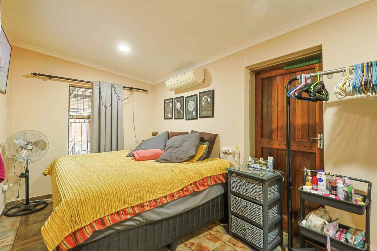 A functional bedroom featuring tiled flooring, a wall-mounted split-system air conditioner, and a solid timber door.