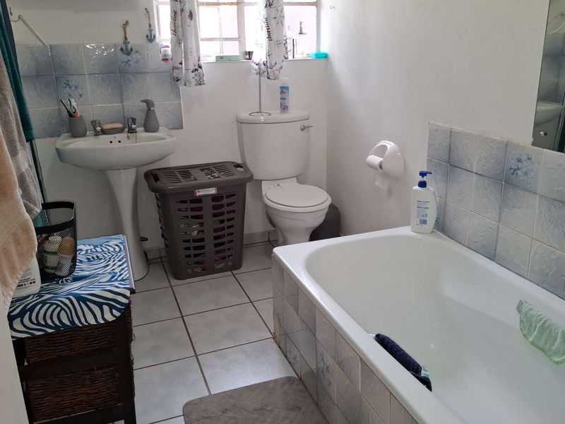 A functional bathroom featuring a pedestal sink, toilet, and bathtub with tiled splashbacks and flooring, offering potential for modernization.