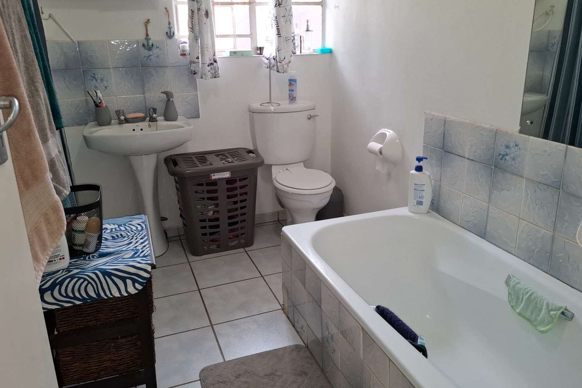 A functional bathroom featuring a pedestal sink, toilet, and bathtub with tiled splashbacks and flooring, offering potential for modernization.