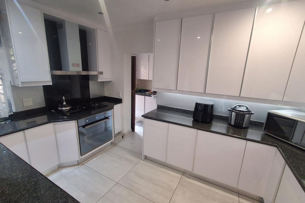 Modern kitchen featuring white cabinetry, dark granite countertops, built-in oven, gas hob, and an extractor fan, with an adjacent scullery area.