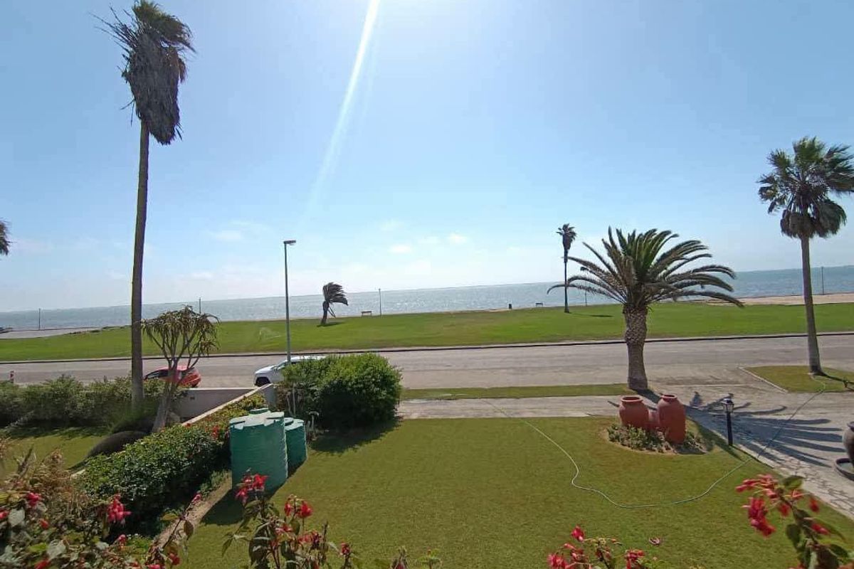 A scenic elevated view overlooking a manicured garden, coastal road, and the ocean horizon.