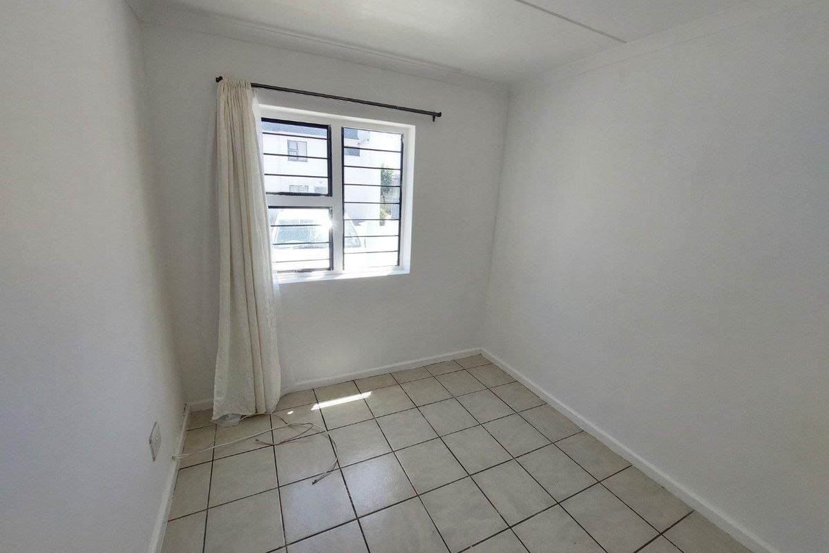 A compact, empty bedroom featuring neutral tiled flooring, white walls, and a window fitted with security bars.
