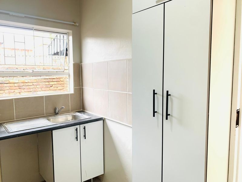 A functional scullery area featuring built-in cabinetry, a stainless steel sink, and tiled splashbacks, providing additional utility space for the apartment.