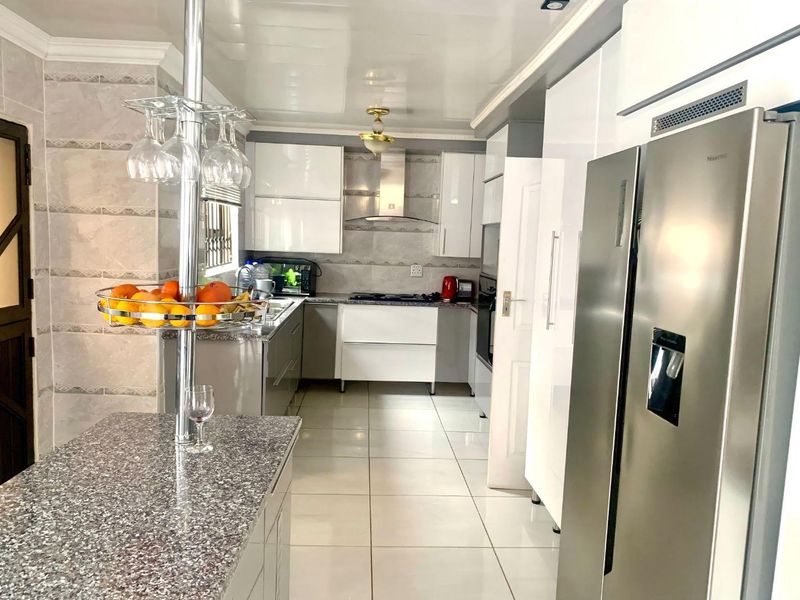 Modern kitchen featuring high-gloss cabinetry, granite countertops, a breakfast bar, and integrated stainless steel appliances with neutral tiled flooring.