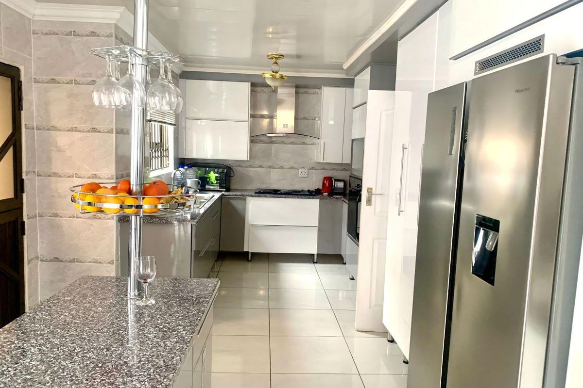 Modern kitchen featuring high-gloss cabinetry, granite countertops, a breakfast bar, and integrated stainless steel appliances with neutral tiled flooring.