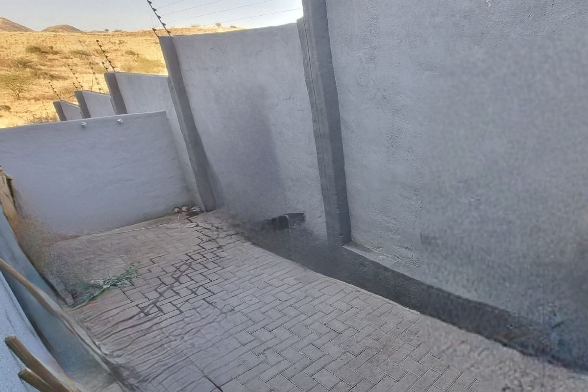 A paved rear courtyard area enclosed by high boundary walls with installed electric fencing.