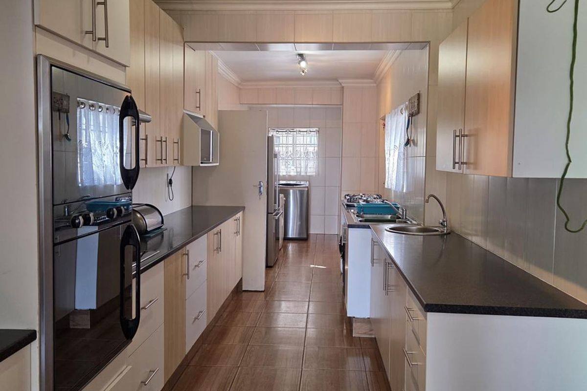 A functional galley-style kitchen featuring built-in cabinetry, integrated oven, hob, and tiled flooring, leading through to a secondary utility or scullery area.