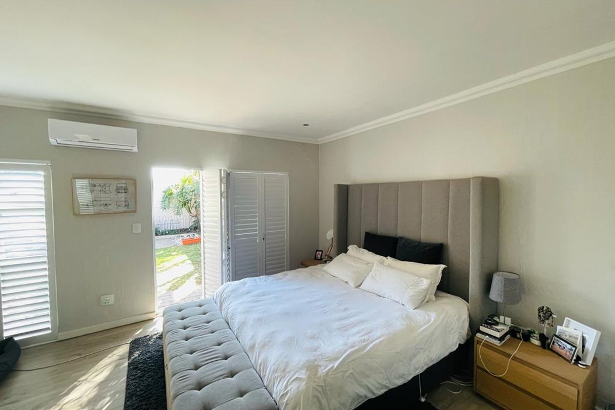 A well-maintained bedroom featuring laminate flooring, a split-system air conditioner, and direct access to the garden through louvered french doors.