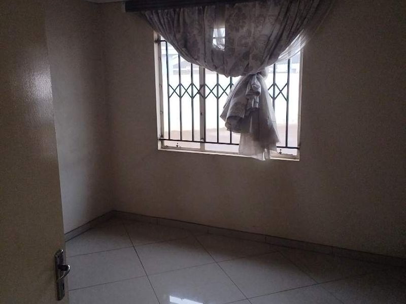 An empty bedroom featuring tiled flooring and a window fitted with security bars.