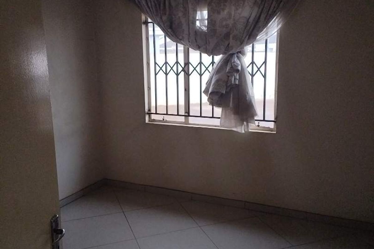 An empty bedroom featuring tiled flooring and a window fitted with security bars.