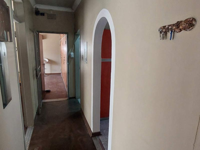A functional hallway featuring an arched doorway and access to adjacent rooms, showing signs of wear and requiring cosmetic updates.