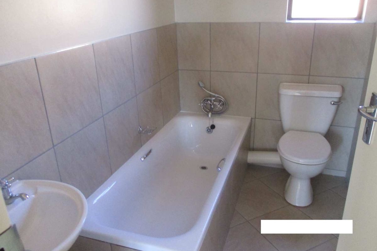 A functional bathroom featuring a bathtub, pedestal basin, and toilet with neutral ceramic tiling throughout.