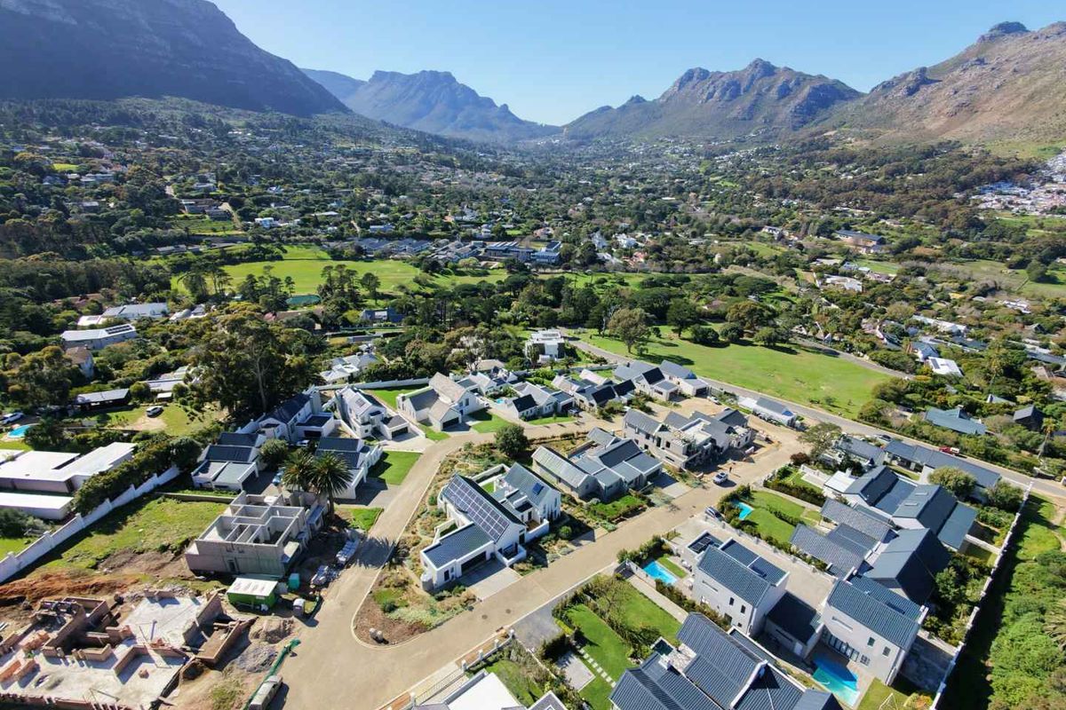 Aerial view of a modern residential estate featuring multiple homes with solar panels, swimming pools, and landscaped gardens set against a mountain backdrop.