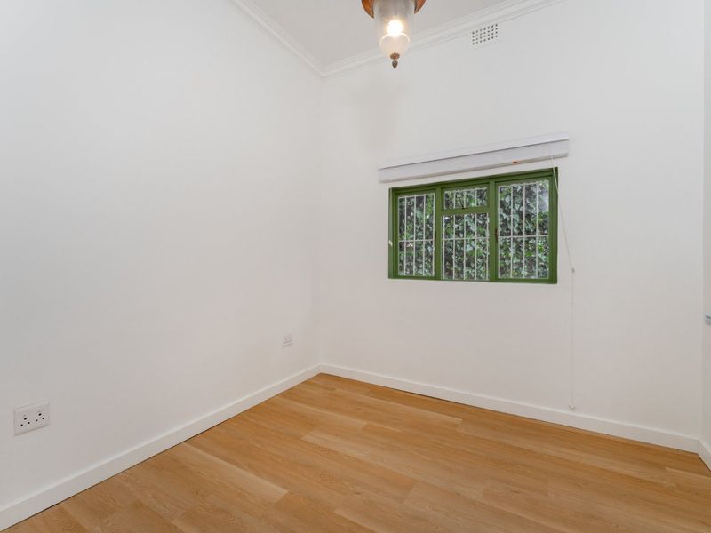 A bright, empty bedroom featuring timber flooring, white walls, and a window fitted with security bars.