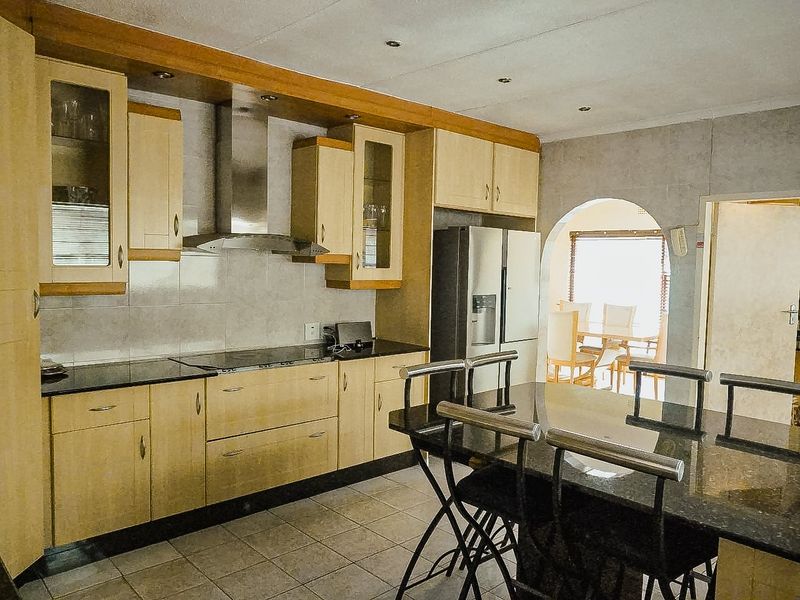 A functional kitchen featuring light wood cabinetry, granite countertops, a stainless steel extractor fan, and tiled flooring, with an open archway leading to the dining area.