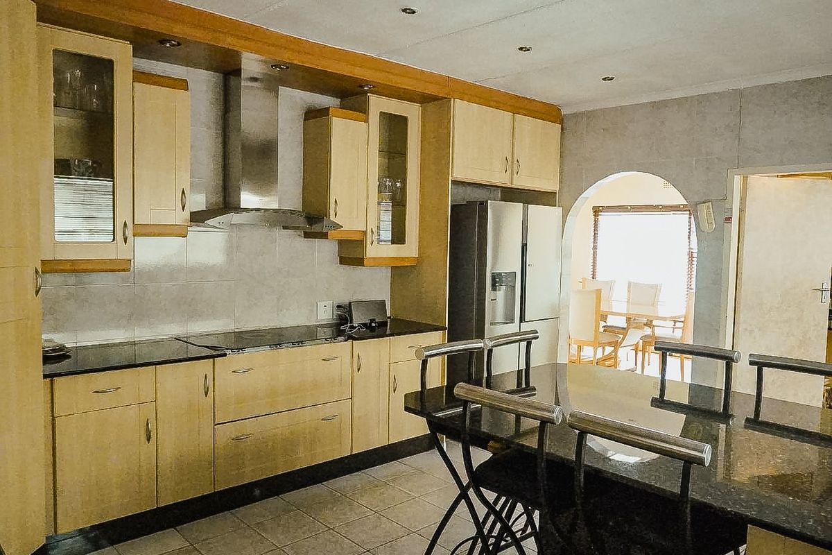 A functional kitchen featuring light wood cabinetry, granite countertops, a stainless steel extractor fan, and tiled flooring, with an open archway leading to the dining area.