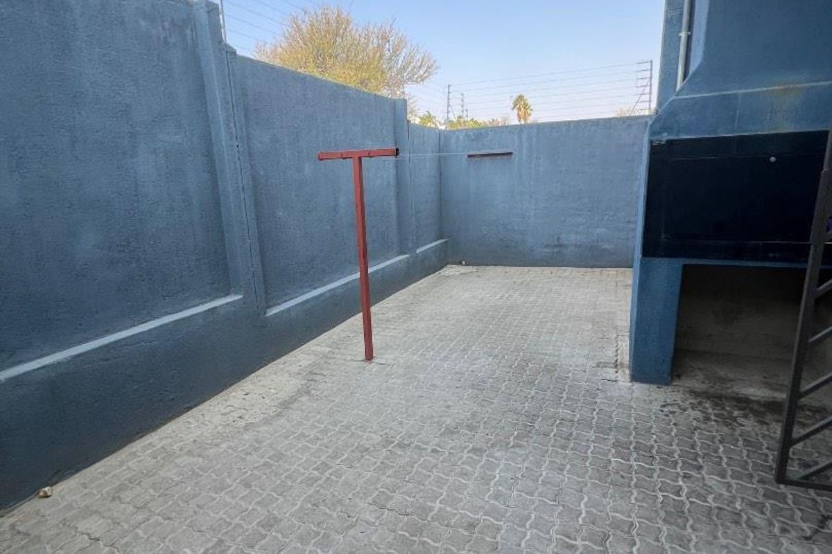 A private rear courtyard featuring paved flooring, a built-in braai area, and perimeter walling with electric fencing.