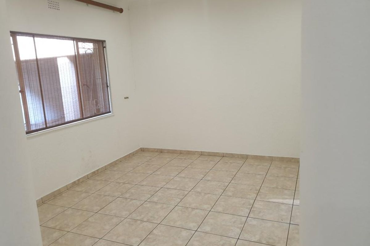 An empty bedroom featuring neutral tiled flooring, a window with security bars, and a curtain rod, providing a blank canvas for personalization.