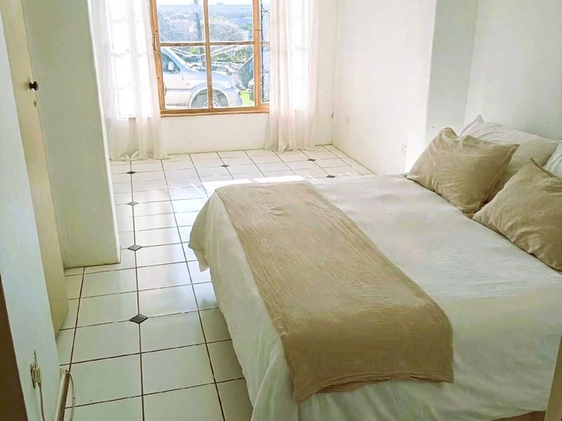 A bedroom featuring tiled flooring and a built-in cupboard, with natural light entering through a large window.