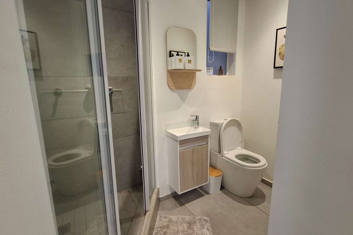Modern bathroom featuring a glass-enclosed shower, wall-mounted vanity with basin, and a contemporary toilet, finished with neutral floor tiles.