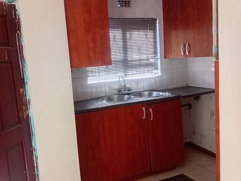 A compact kitchen featuring wooden cabinetry, a double bowl sink, and tiled flooring, currently in need of maintenance and cosmetic updates.