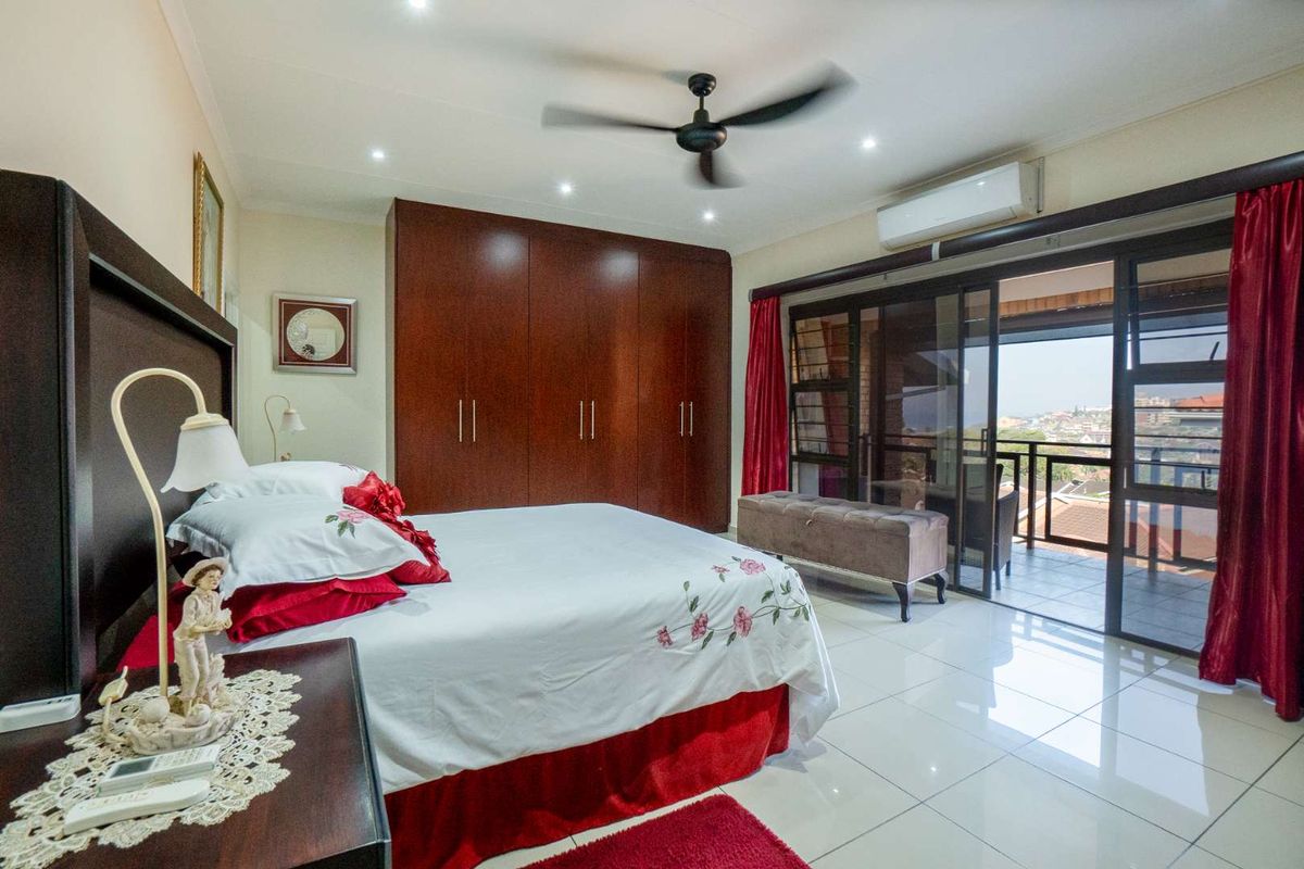 Spacious bedroom featuring built-in wooden cupboards, tiled flooring, a ceiling fan, air conditioning unit, and sliding glass doors leading to a private balcony.
