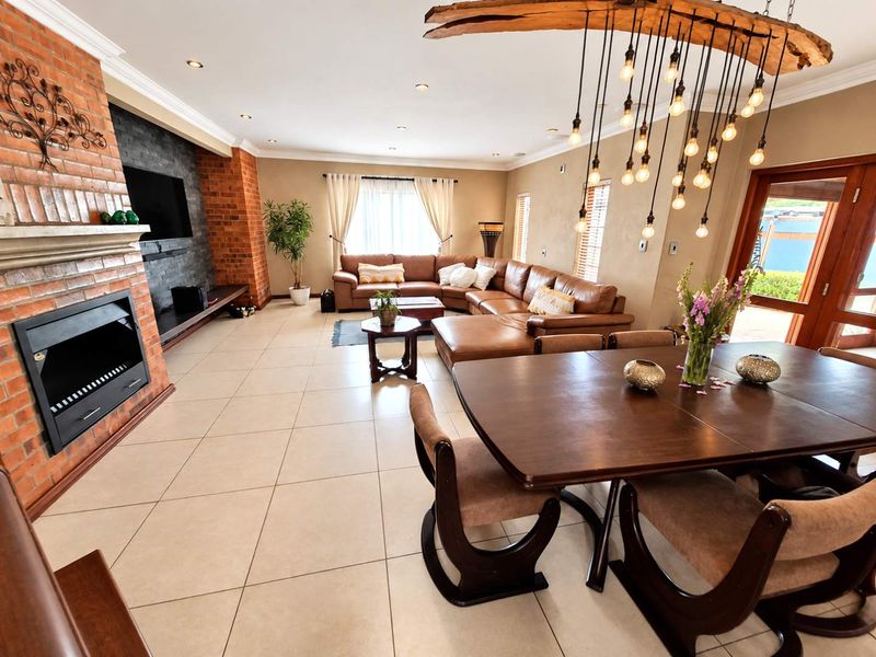 Spacious open-plan living and dining area featuring a prominent exposed brick fireplace, tiled flooring, and modern recessed lighting throughout.
