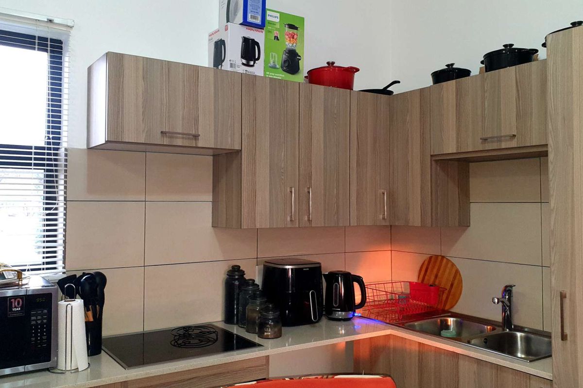 Compact kitchen featuring modern wood-look cabinetry, stone countertops, an integrated induction hob, and a stainless steel sink with tiled splashbacks.