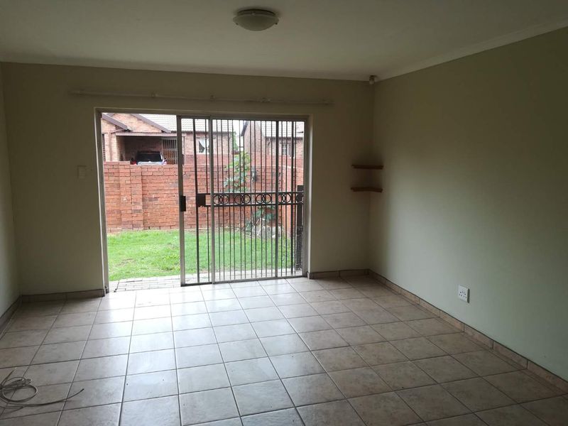 An empty living room featuring ceramic floor tiles and a sliding glass door with a security gate, providing direct access to the rear garden.